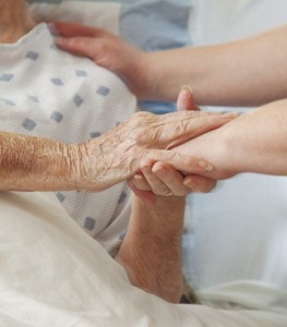 Senior woman in hospital bed being comforted by caretaker